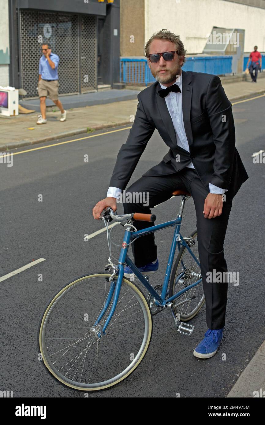 man dressed in tuxedo standing beside bicycle Stock Photo