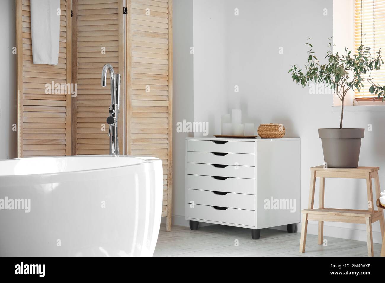 Modern bathtub and chest of drawers near white wall in bathroom
