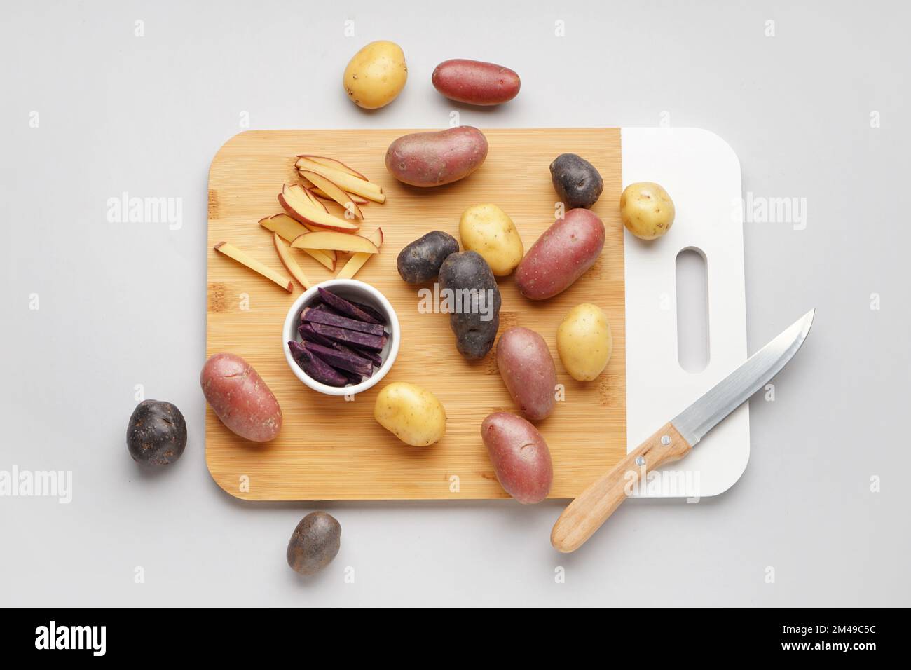 https://c8.alamy.com/comp/2M49C5C/wooden-board-with-different-raw-potatoes-and-knife-on-light-background-2M49C5C.jpg