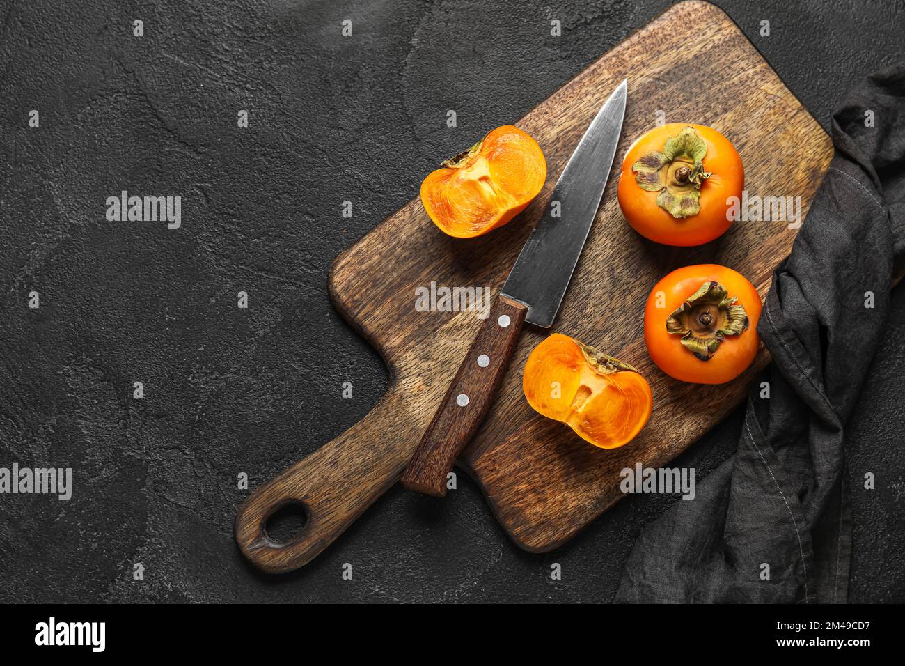 Wooden board with fresh ripe persimmons and knife on dark background Stock Photo
