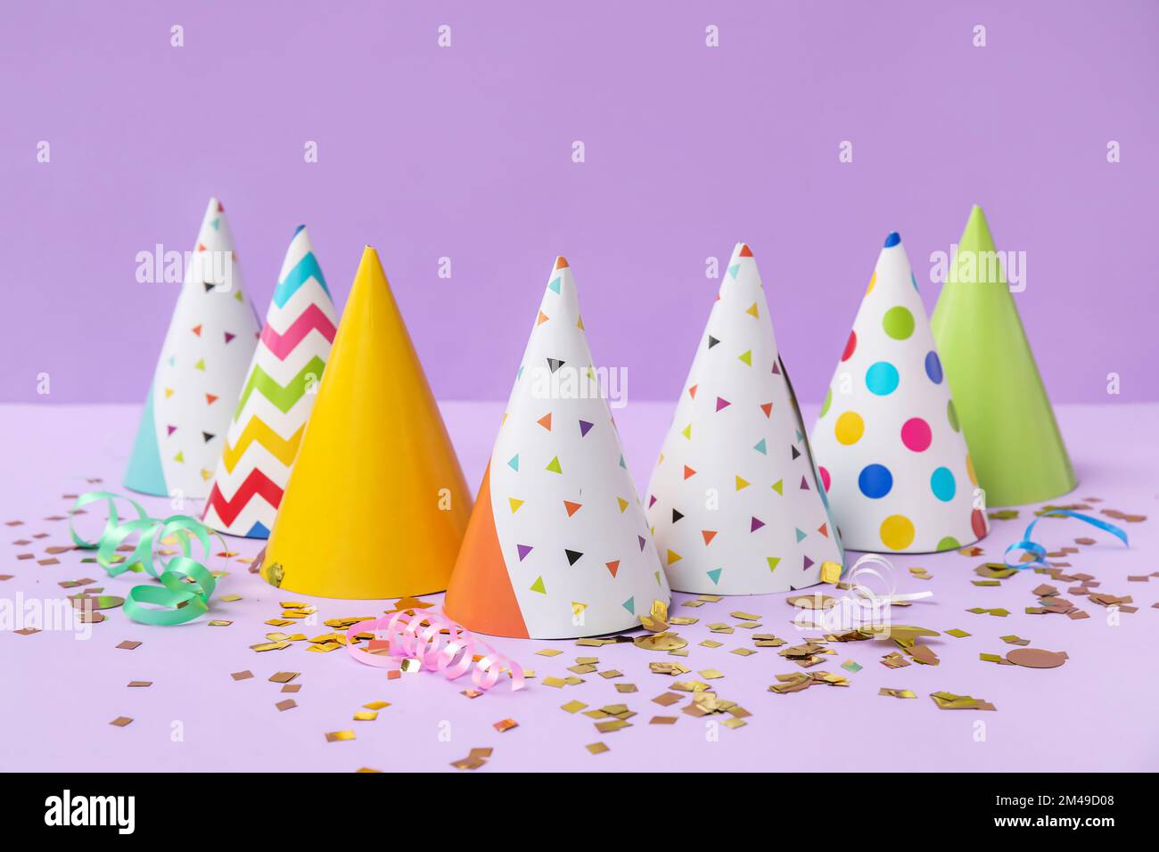 Party hats and confetti on lilac background Stock Photo - Alamy