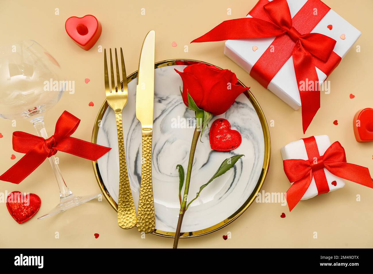 Table setting for Valentine's Day with red rose and gifts on beige ...