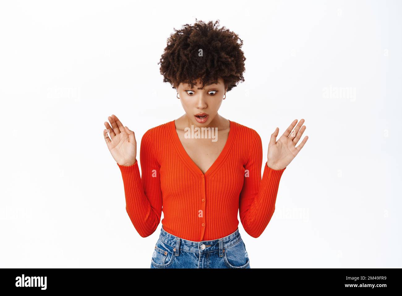 Shocked woman drops smth down, looks below with startled face and