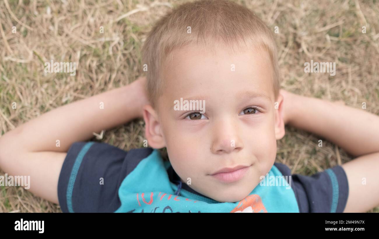 Little Happy Serious and Thoughtful Child Boy Laying on Yellow Lawn Dry