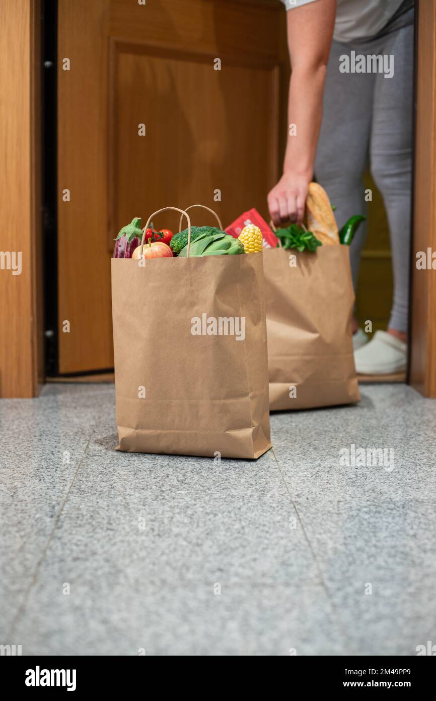 A woman picks up a bag of food at the door of her house. Coronavirus