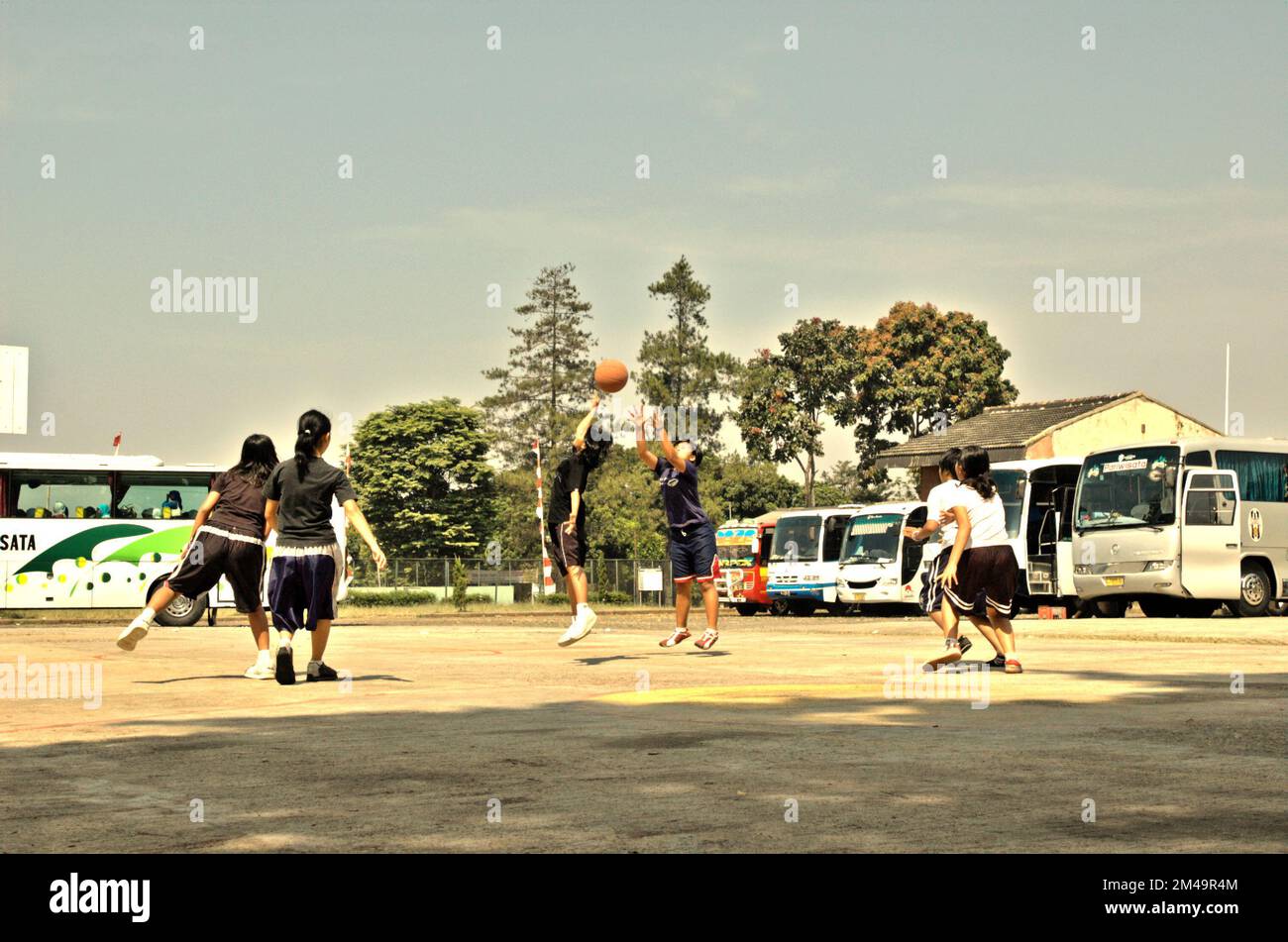 Teenagers playing basketball at a basketball field that occasionally also functioned as a parking ground for buses carrying religious tourists who want to visit Daarut Tauhiid area in Gegerkalong, Bandung, West Java, Indonesia. Stock Photo