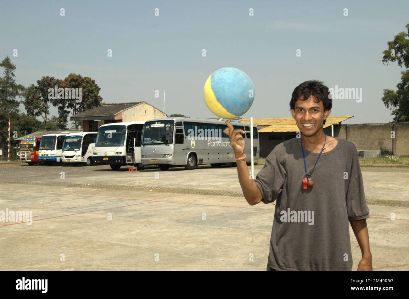 A young coach playing basketball at a basketball field that occasionally also functioned as a parking ground for buses carrying religious tourists who want to visit Daarut Tauhiid area in Gegerkalong, Bandung, West Java, Indonesia. Stock Photo