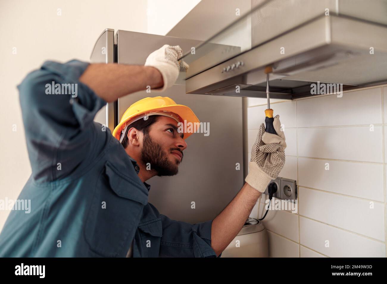 Handyman in uniform repairing kitchen extractor, replacing filter in