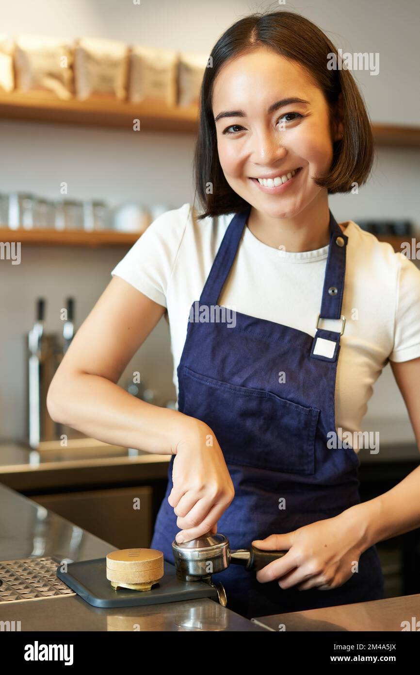 Vertical shot of barista, asian girl in cafe using tamper for coffee