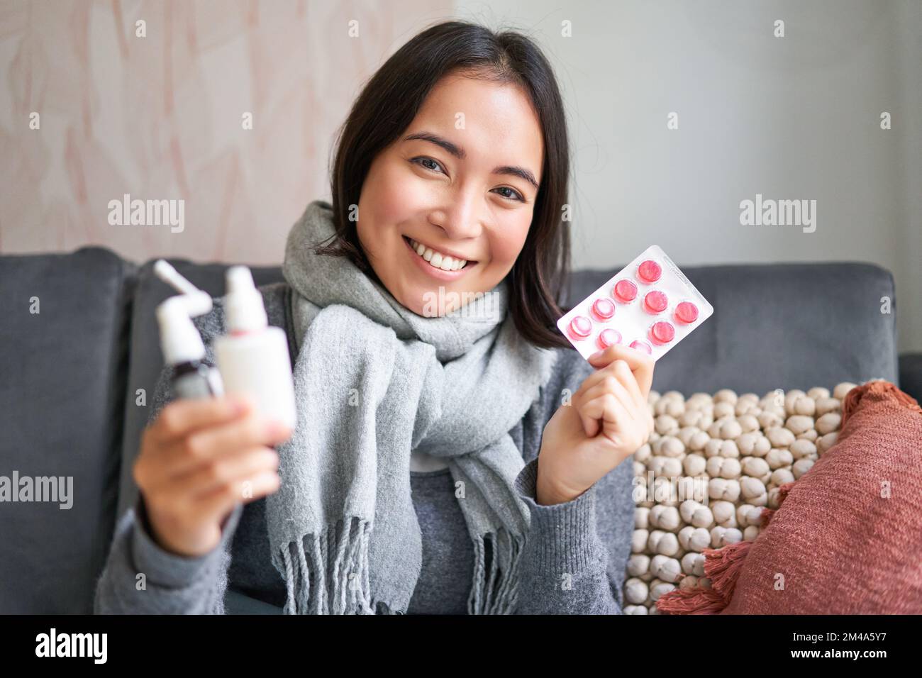 Portrait of happy smiling asian girl showing medication, sore throat spray and drugs from flu or