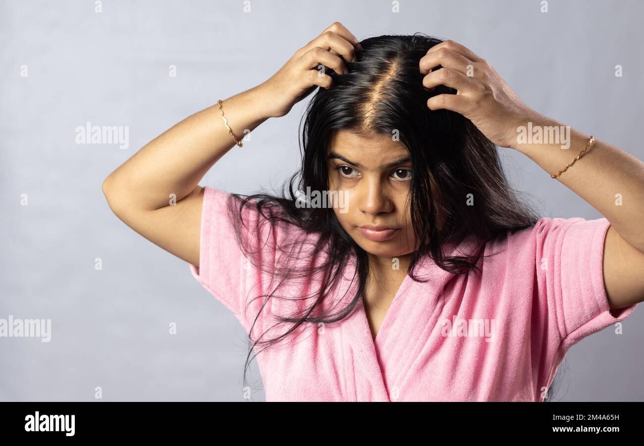 An Indian woman worried due to hair loss problem holds scalp on white background Stock Photo