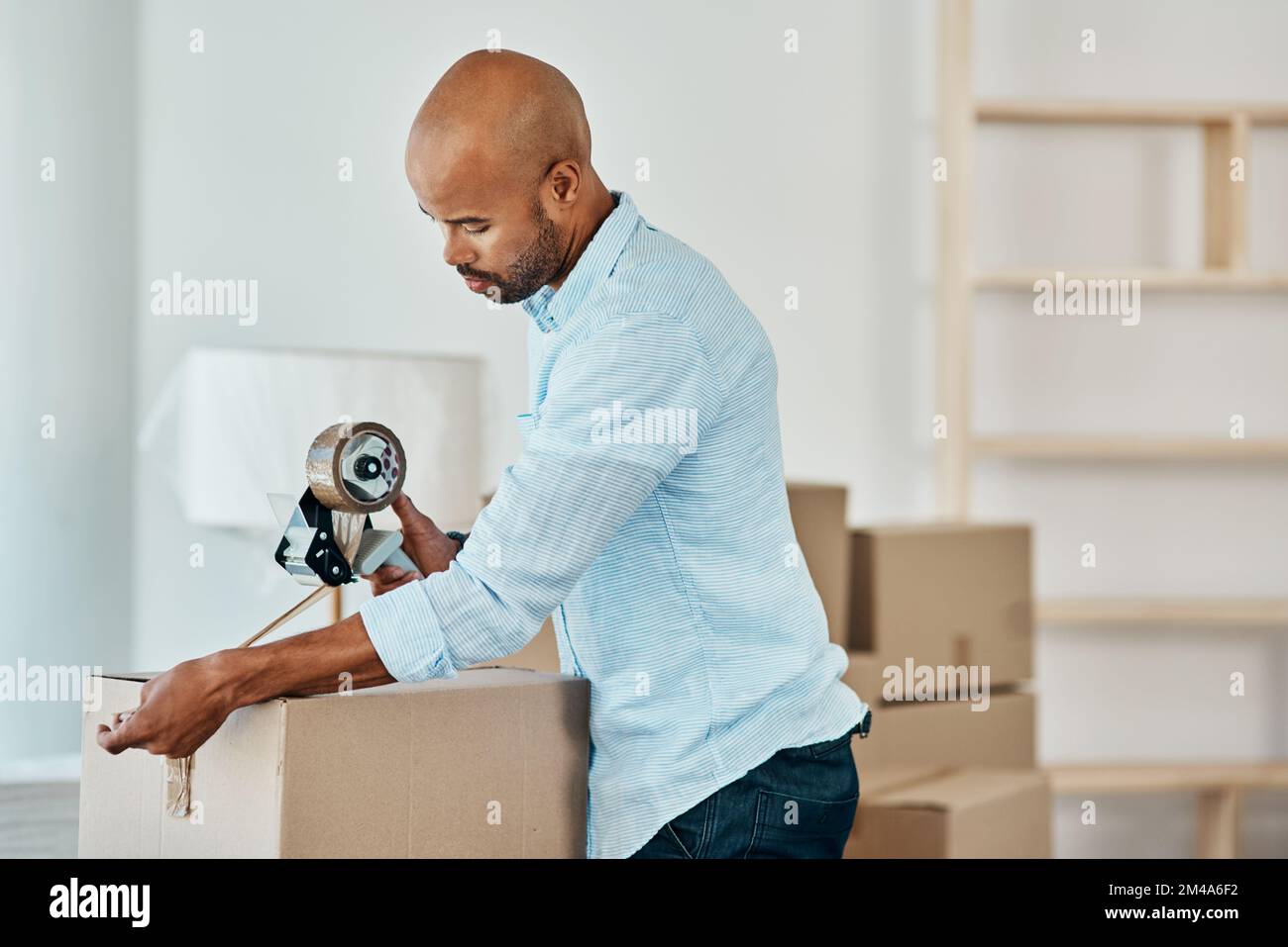 Its time to move on. Shot young man sealing a box while moving house