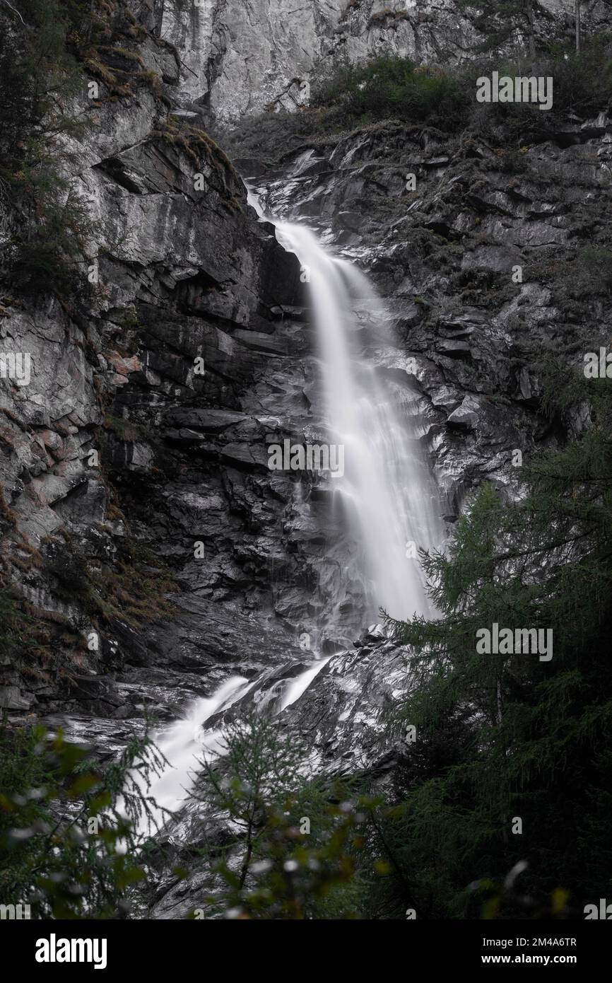 A vertical long exposure shot of a waterfall flowing between rocky ...