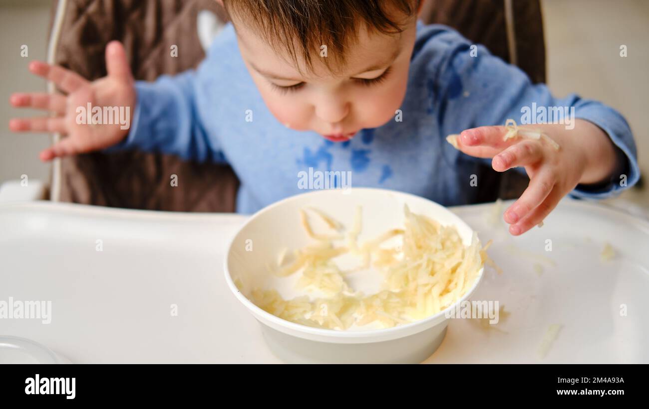 Funny child eating a grated apple with his hand from a plate, closeup