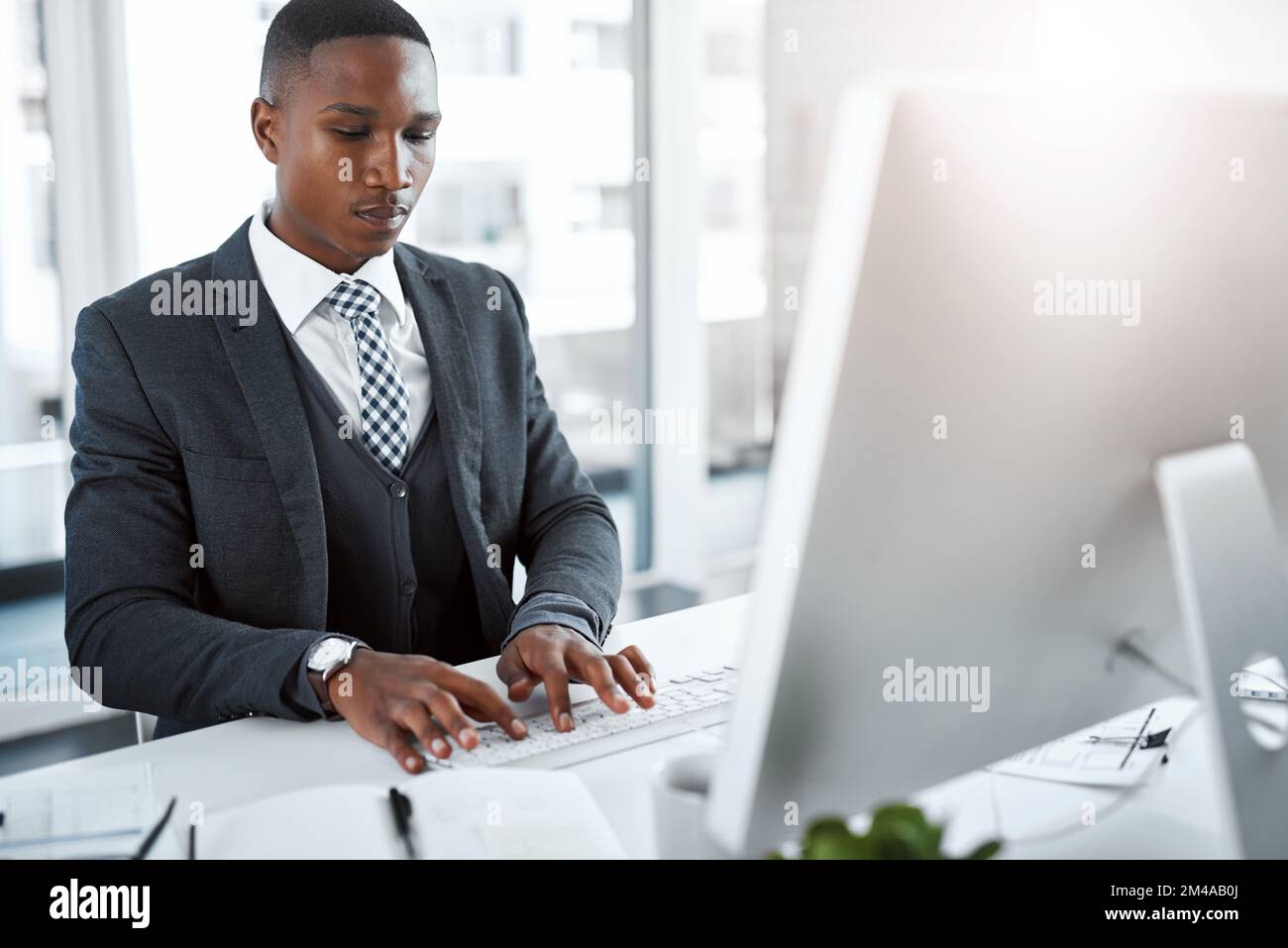 Hell make it work no matter what. a young businessman using a computer at his desk in a modern office. Stock Photo