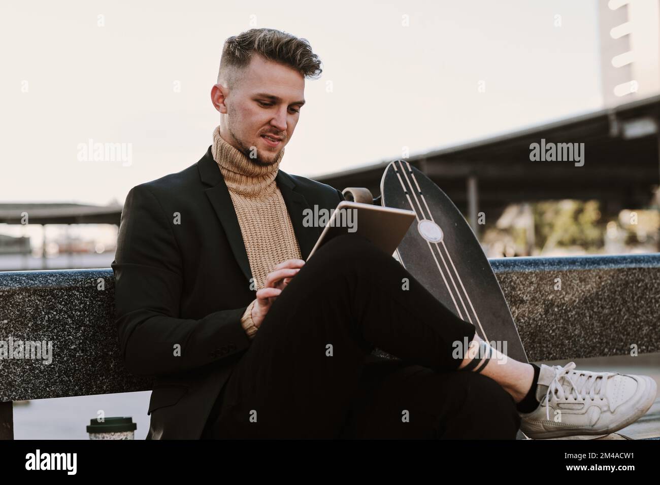 Man using a tablet while sitting next to a skateboard Stock Photo