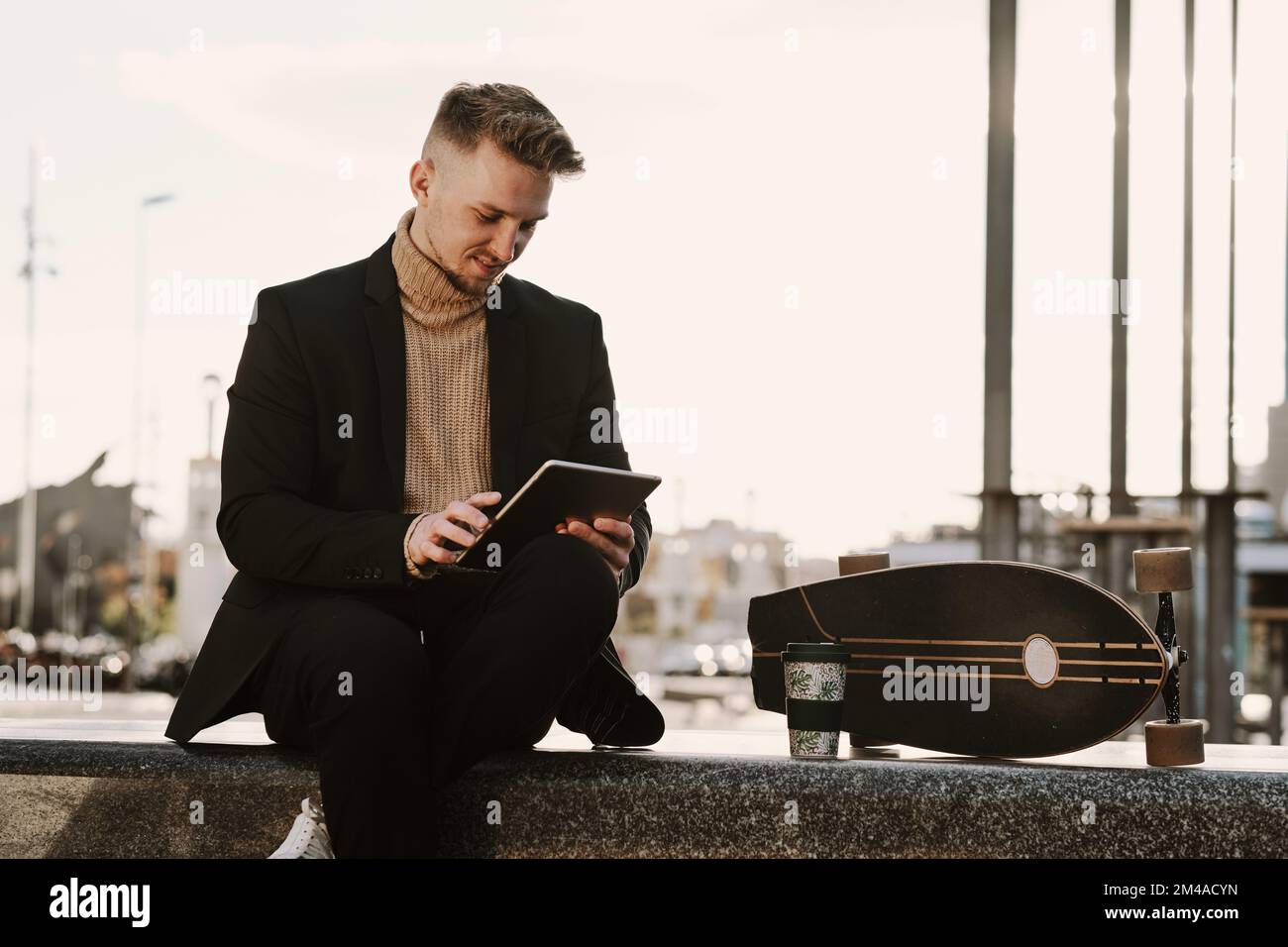 Stylish skater using a tablet sitting in a square Stock Photo