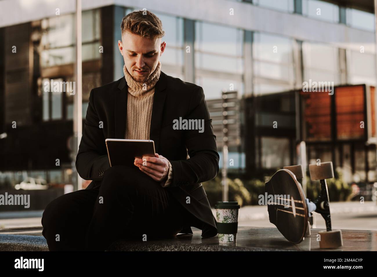 Stylish man using a tablet sitting next to a skateboard Stock Photo