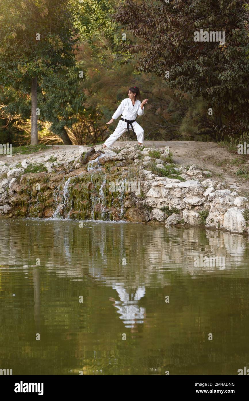 Sporty woman in kimono and black belt training karate in the nature. Sports and martial arts concept. Stock Photo