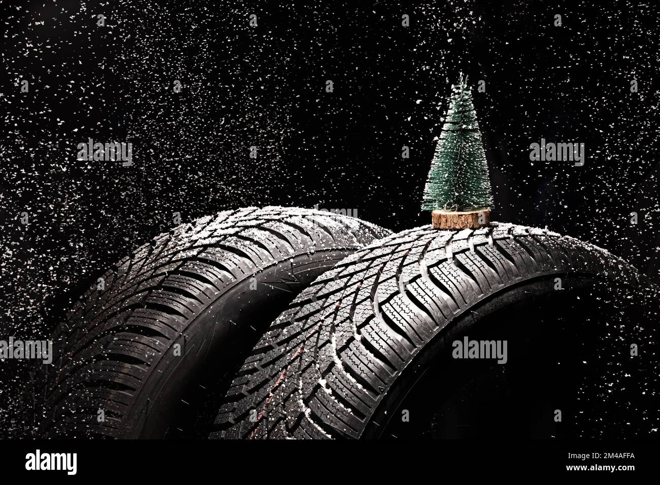 Winter Car tire for snow, forest pine tree and snowflakes isolated on black background. New automobile tyre for snowy road. Stock Photo
