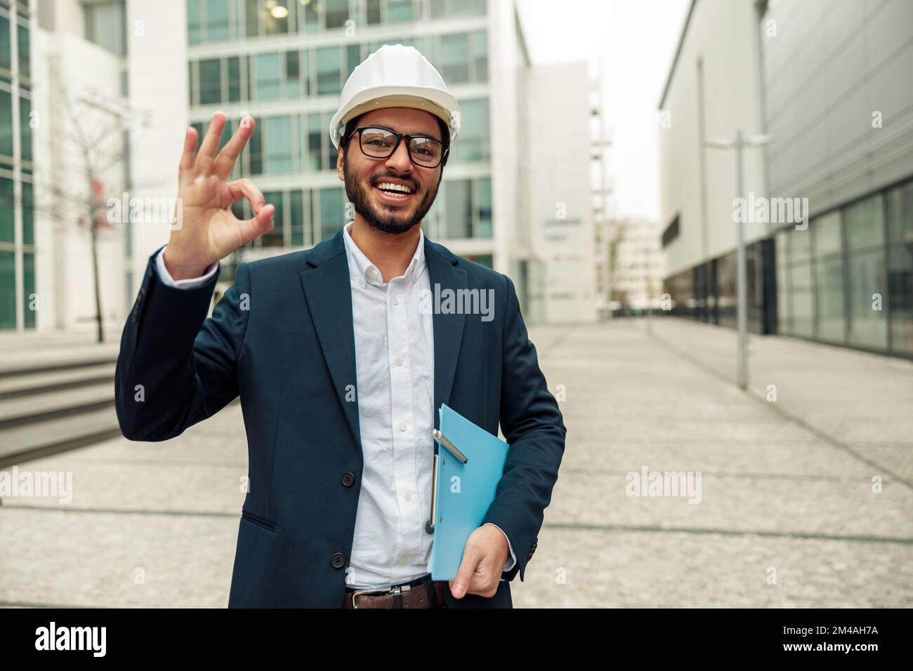 Indian construction architect in suit and hardhat with paper folder in hands against modern building Stock Photo
