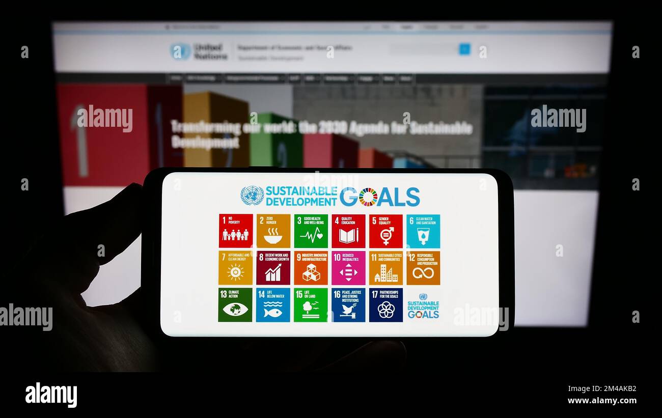 Person holding smartphone with logo of UN Sustainable Development Goals (SDG) on screen in front of website. Focus on phone display. Stock Photo