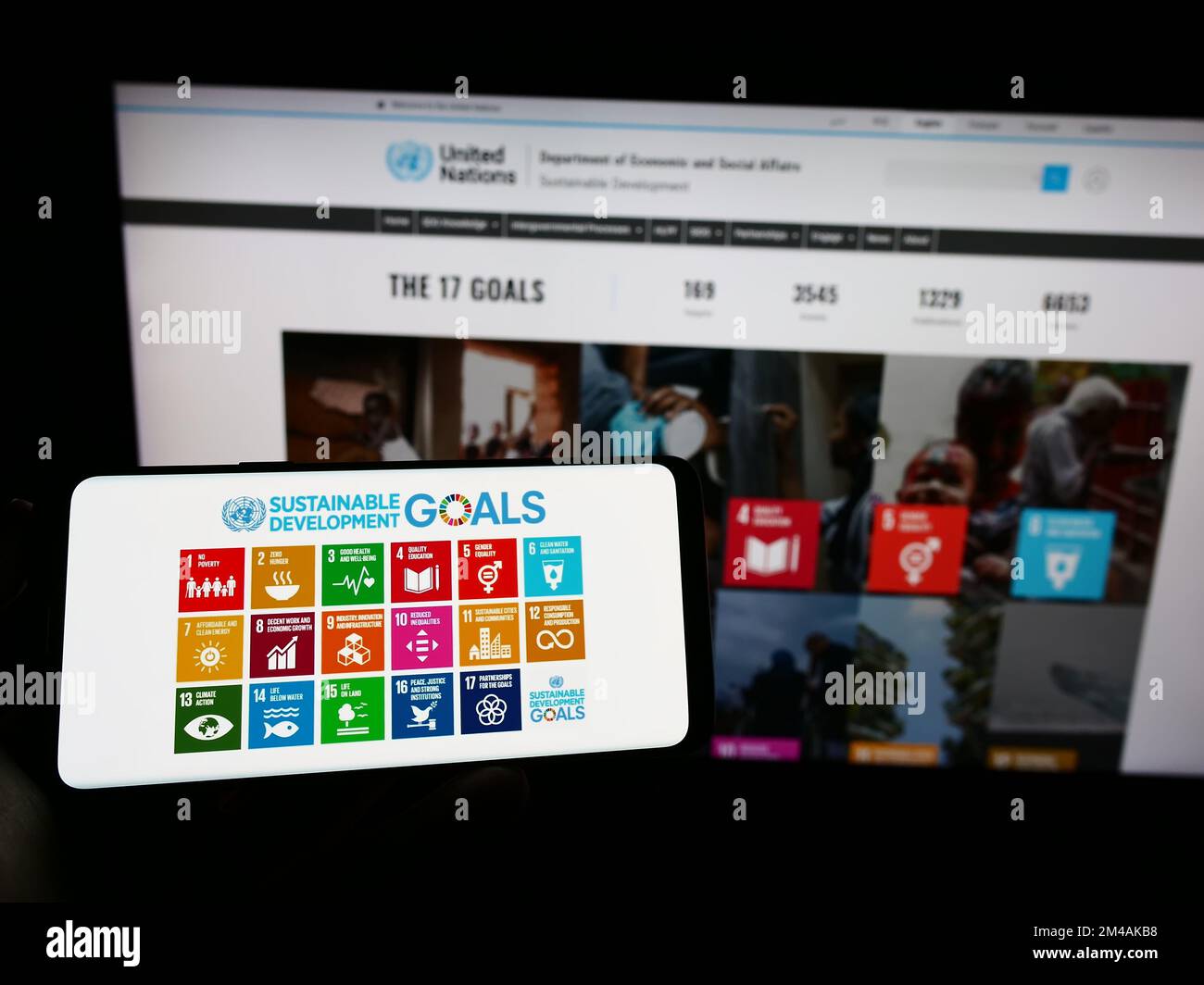 Person holding cellphone with logo of United Nations Sustainable Development Goals (SDG) on screen in front of webpage. Focus on phone display. Stock Photo