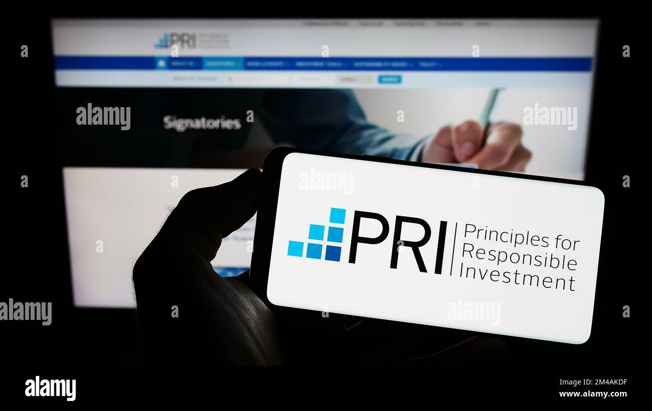 Person holding cellphone with logo of UN Principles for Responsible Investment (PRI) on screen in front of webpage. Focus on phone display. Stock Photo