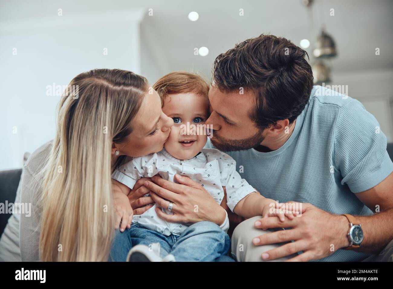 Mom, dad and baby kiss on sofa in living room of happy family home ...