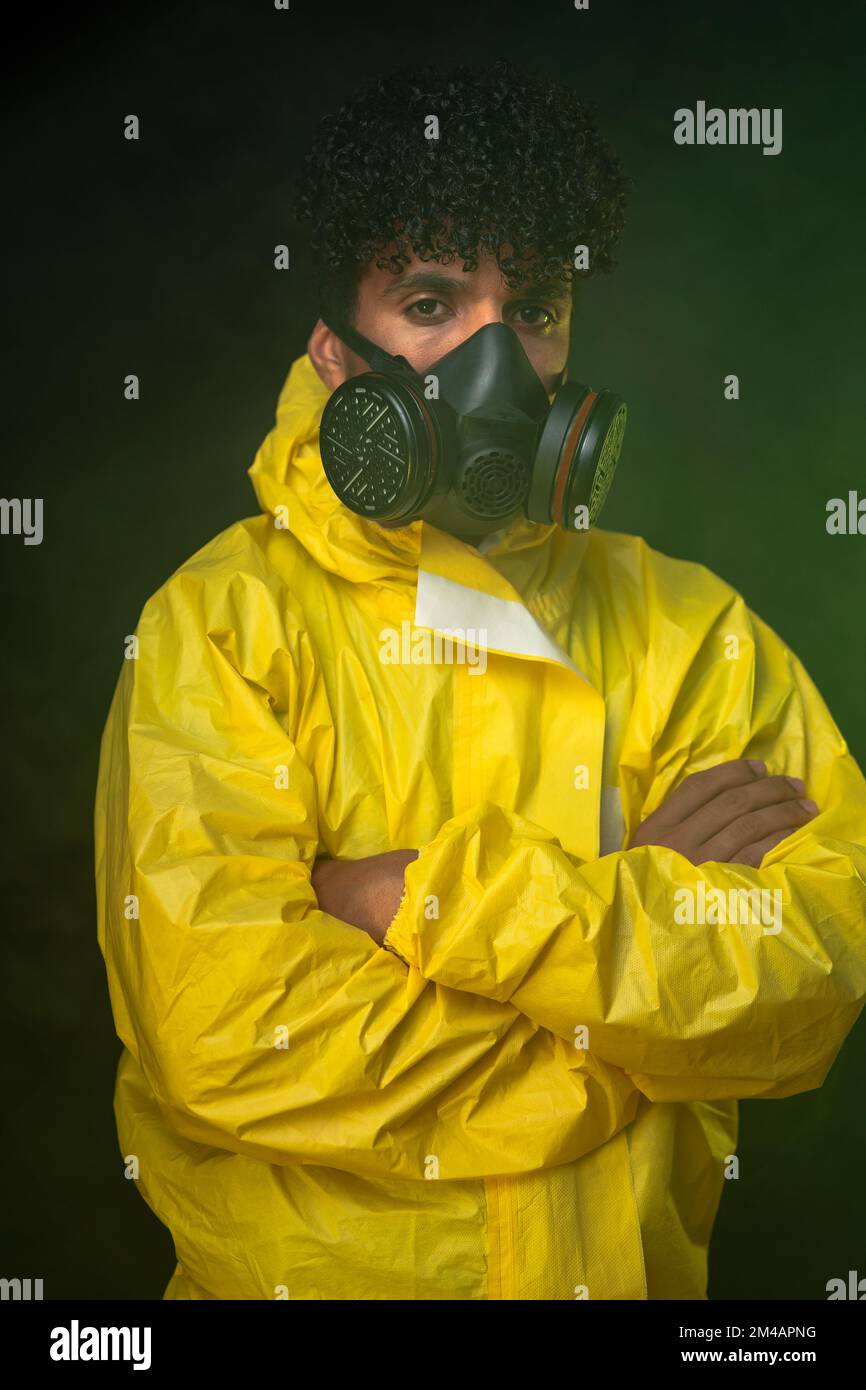 Young Hispanic man in yellow hazmat suit and respirator looking at