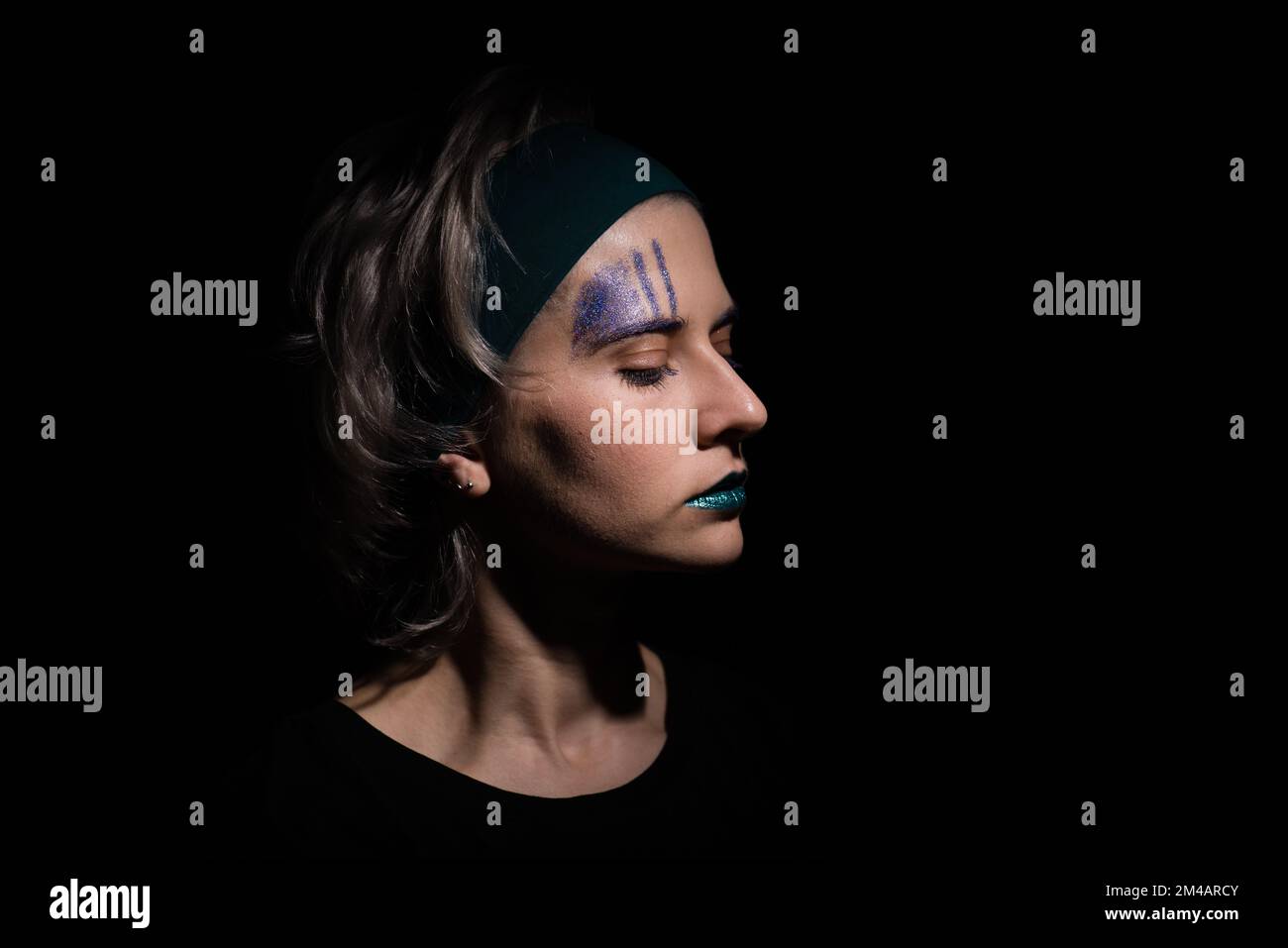 dark dramatic female portrait with trendy teal color lipstic. blond hair woman looking down, mysterious portrait of woman on dark background Stock Photo