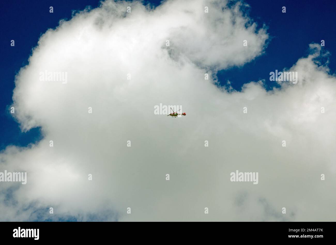 View from the ground of the London Air Ambulance flying overhead on a sunny day with white fluffy clouds and blue sky.  The helicopter swiftly takes p Stock Photo