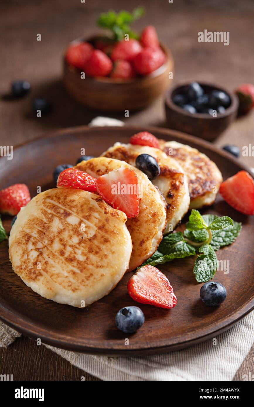 Cottage cheese pancakes or syrniki  with mint, strawberries and blueberries on a dark wooden table. Concept of healthy breakfast. Macro and selective Stock Photo