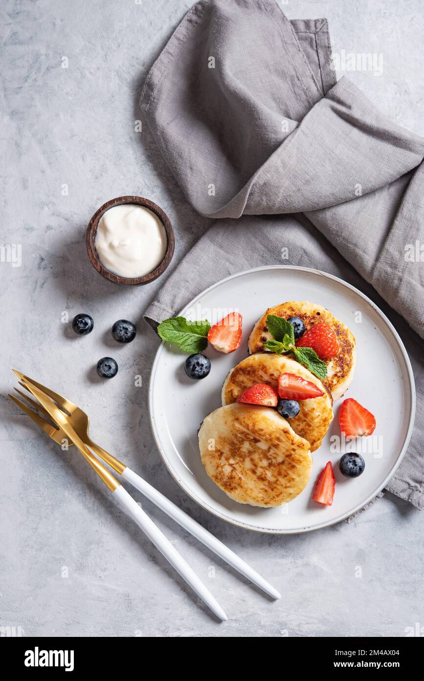 Traditional Russian dish for breakfast  syrniki. Cottage cheese pancakes with sour cream and fresh berries on a blue background with tableware and nap Stock Photo