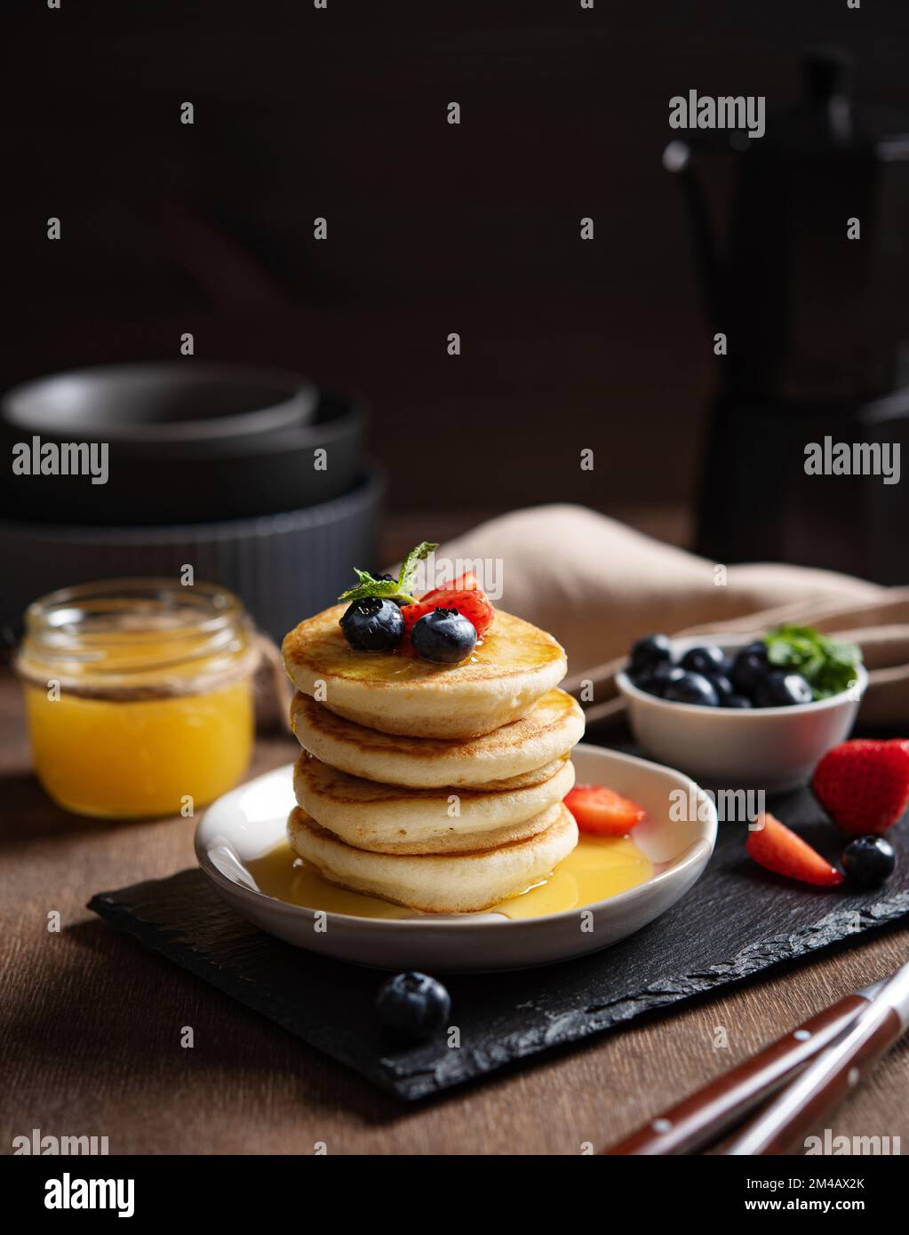 Delicious homemade pancakes with strawberries and blueberries and honey on a dark wooden background with coffee pot. The concept of a healthy and nutr Stock Photo