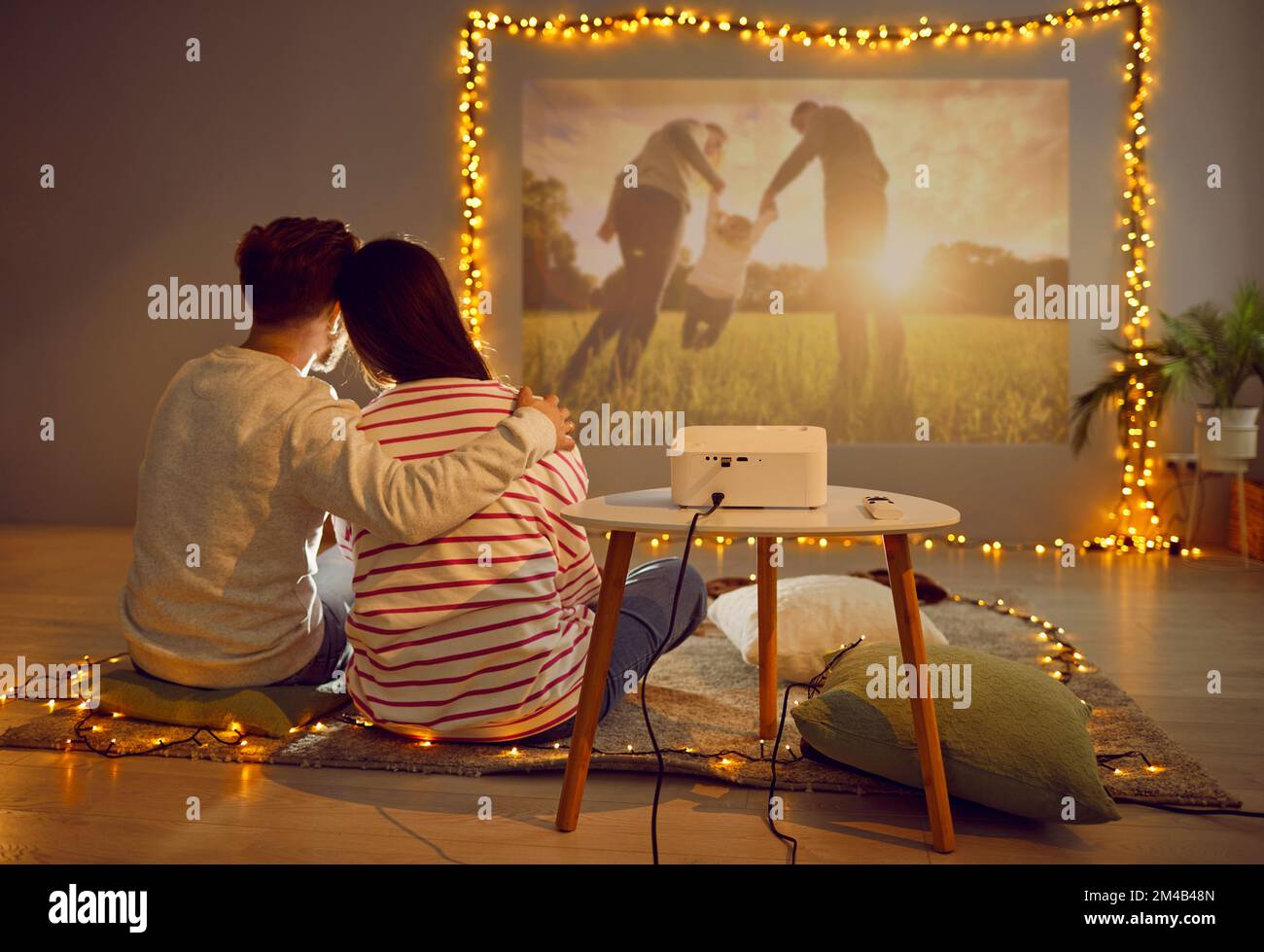 Happy loving couple having romantic date at home, sitting on floor and watching movie on projector Stock Photo