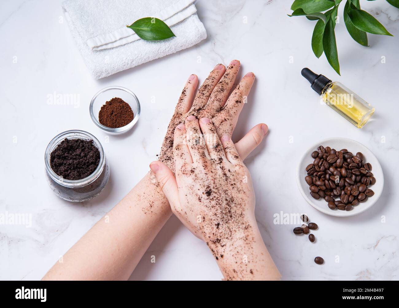 Home spa care for the skin of hands and nails. A young woman does a hand massage with a homemade coffee scrub with olive oil on marble background. Top Stock Photo
