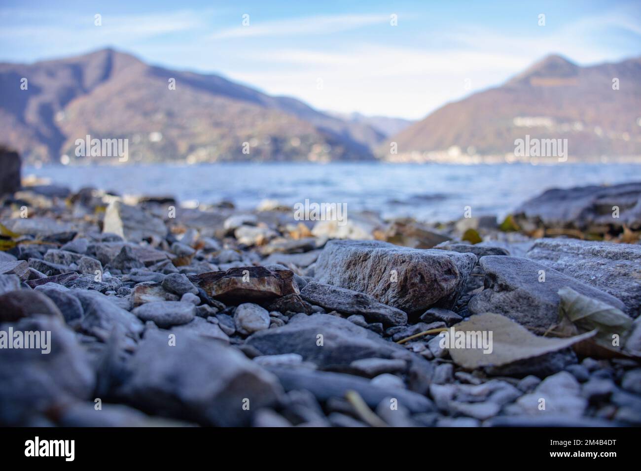 Low Angle View of Gravel beach with tree trunks on Maggiore Lake. Luino, Italy Stock Photo