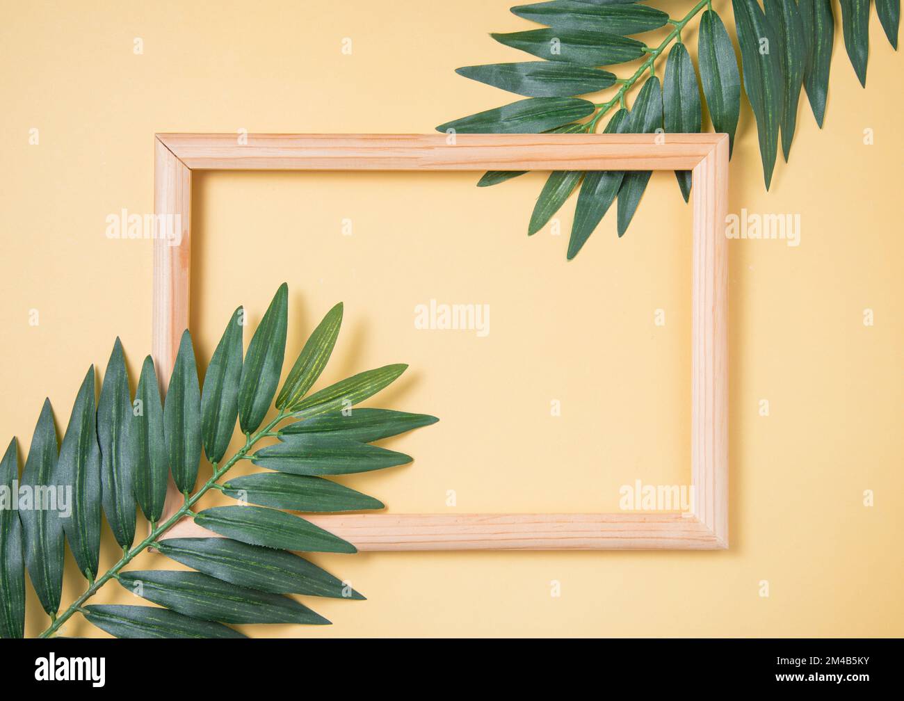 Two palm tree leaf and wooden frame on yellow background. Top view and space for text Stock Photo