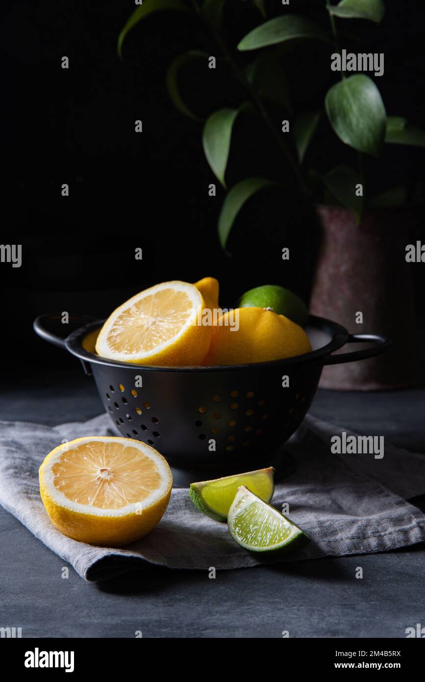 juicy lemons and limes in a black bowl on a gray table. Dark and mood concept. front view Stock Photo