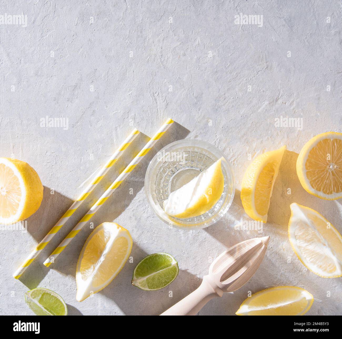 juicy slices of lemon and lime and a glass of mineral water with lemon on a white table with hard morning shadows. Top view and copy space Stock Photo