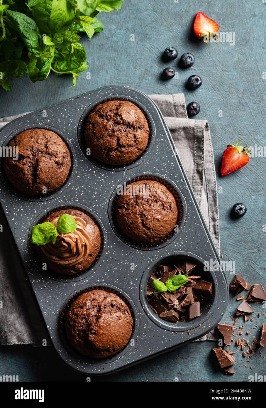 chocolate muffins with blueberry and strawberry slices in a baking dish on a dark  background. Top view. Stock Photo