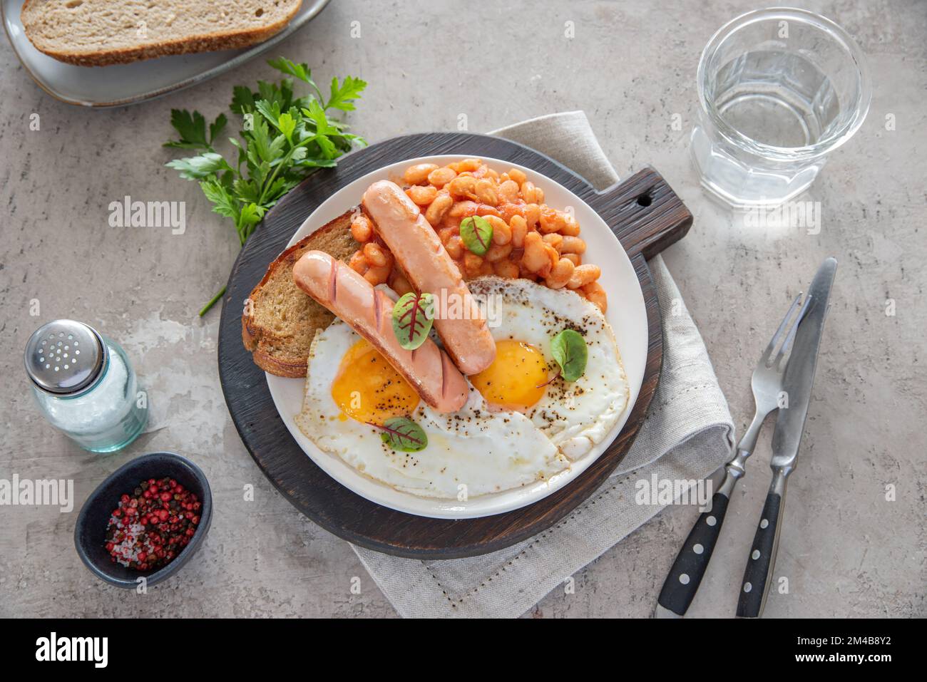 Traditional English breakfast with fried eggs, sausages, beans, fresh herb, red pepper and toast on a gray background. Concept morning and nutrition f Stock Photo