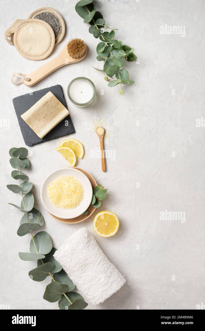 Flat lay organic yellow sea salt with lemon,  soap,  brush, sponge and eucalyptus branch  on a white textured background. The concept of spa and welln Stock Photo