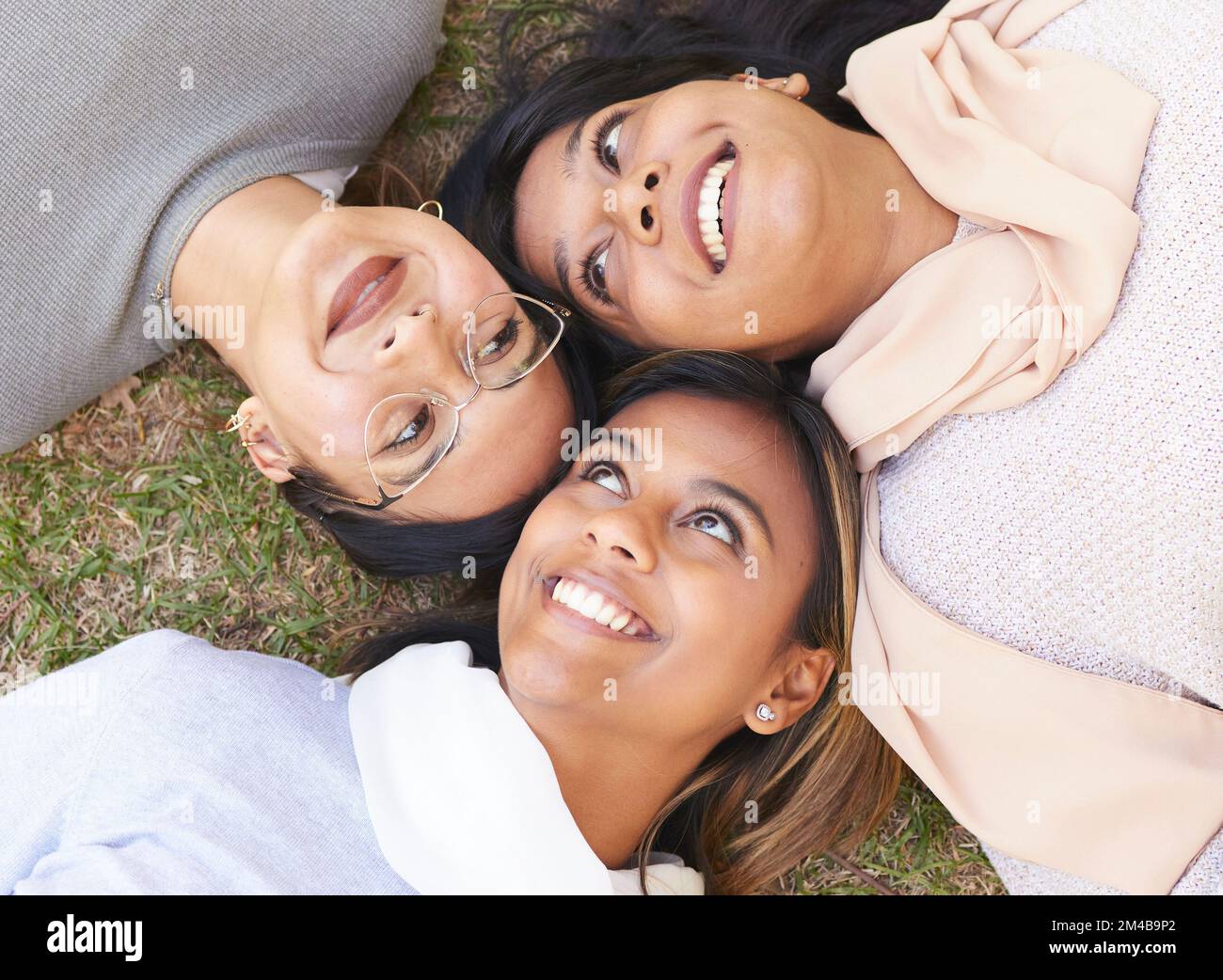 Faces, group and women lying on the ground in a park for cheerful bonding with love and care. Friendship, overhead and female hangout in a garden Stock Photo