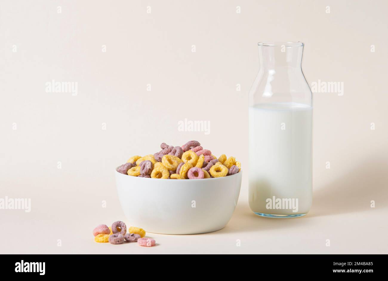 sweet colorful cornflakes rings in a white bowl with a bottle of milk on a yellow background. Front view and copy space image Stock Photo