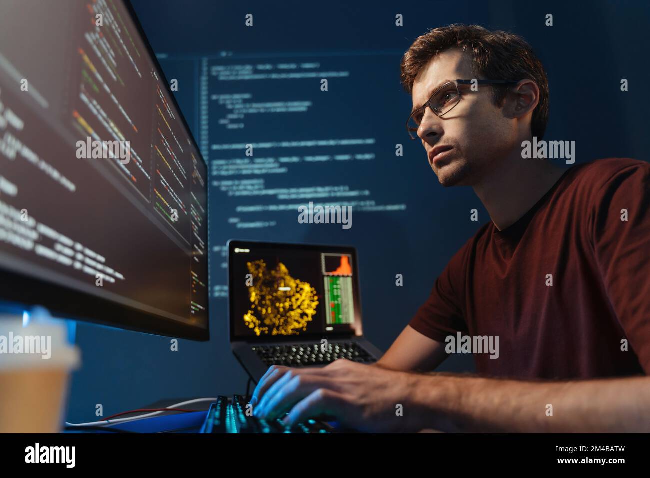 Closeup portrait of handsome IT support specialist monitoring feedback and complaints of online application users, sitting at big pc screen, typing, wearing glasses and red t-shirt Stock Photo