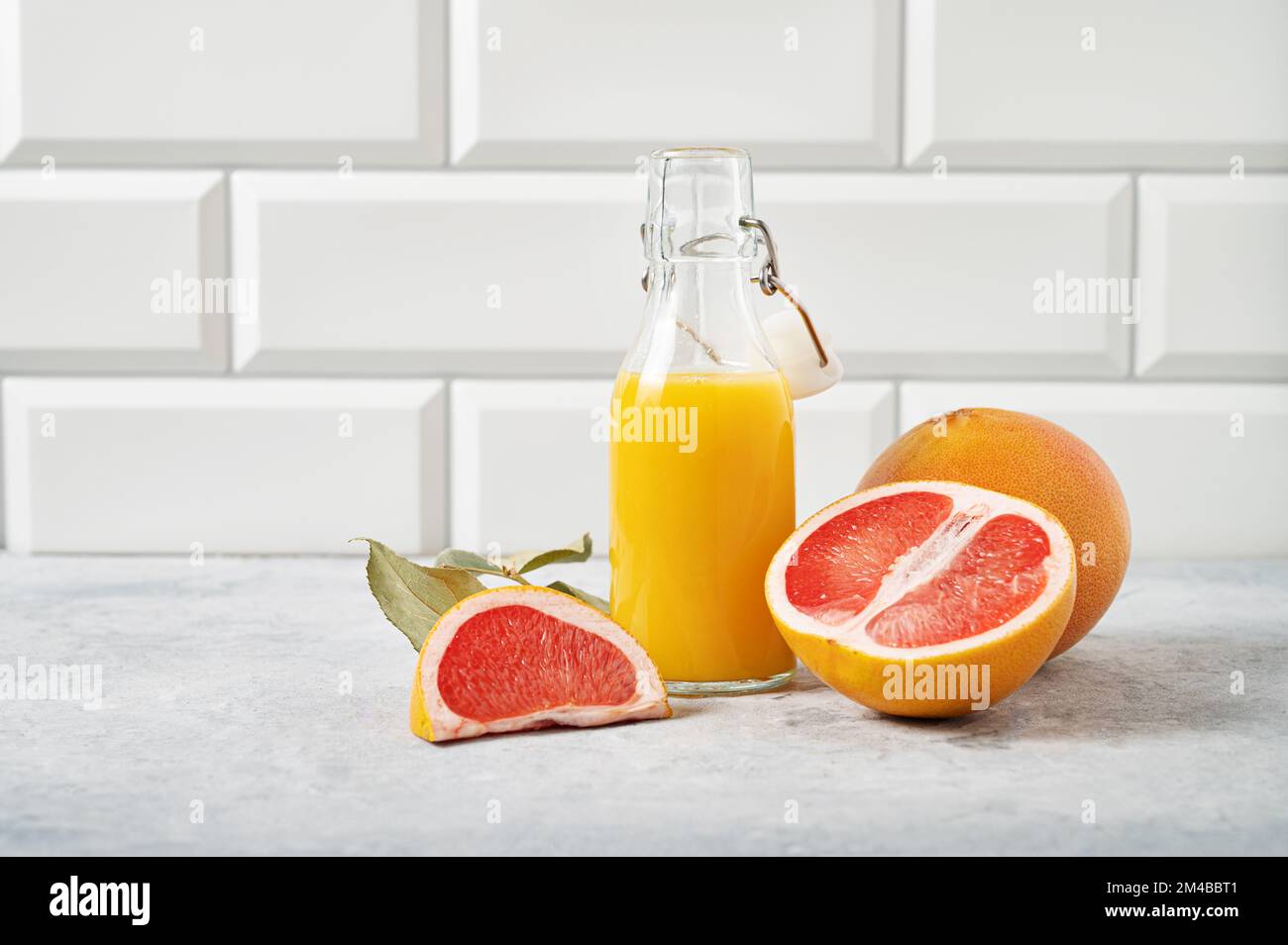 juicy grapefruit and bottle juice on a blue table on  a white brick background. Front view and copy space. Stock Photo