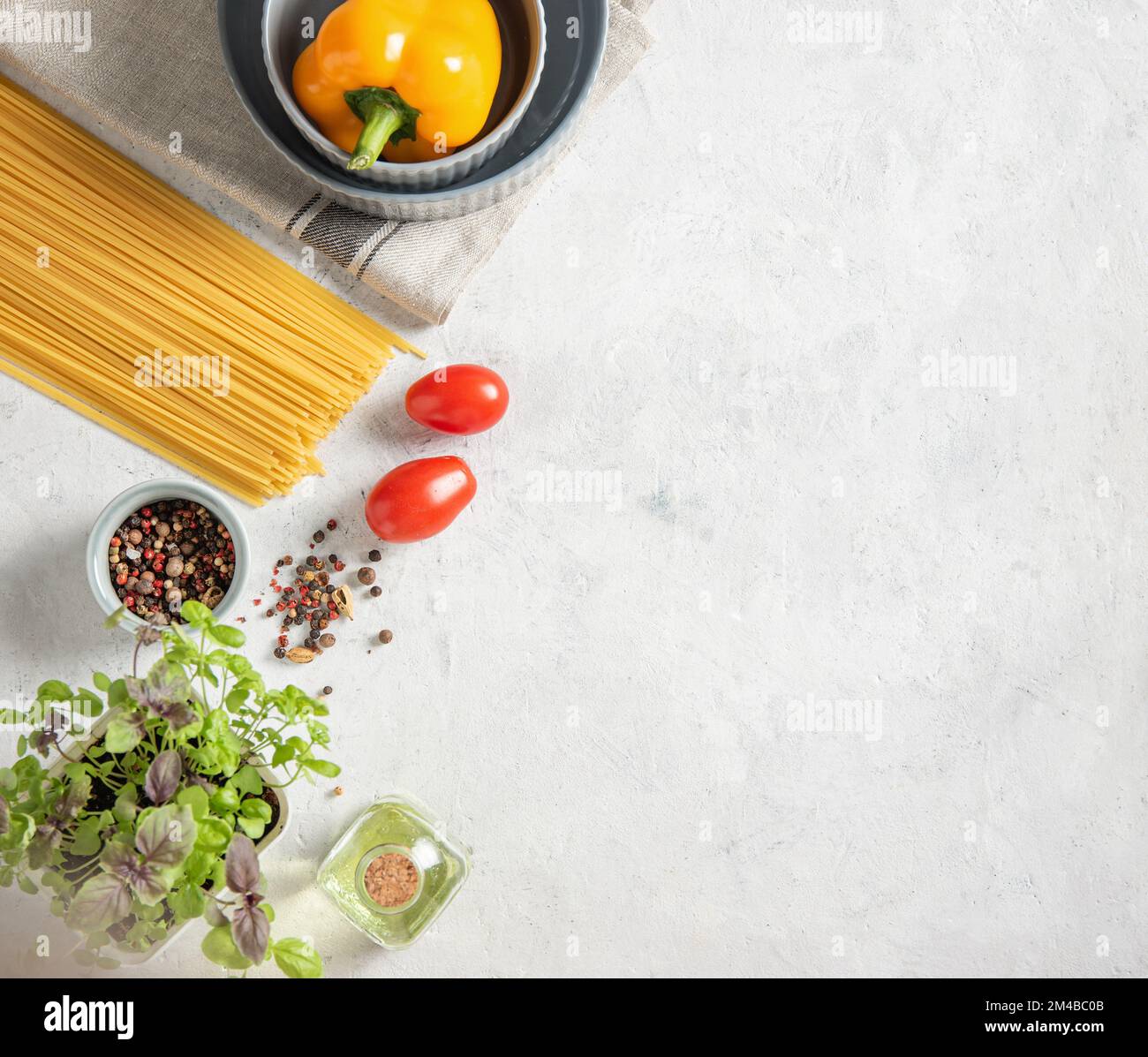 Consept flat lay with raw spaghetti with tomatoes, basil, pepper and olive oil on a white brick background. Traditional ingredients for making Italian Stock Photo