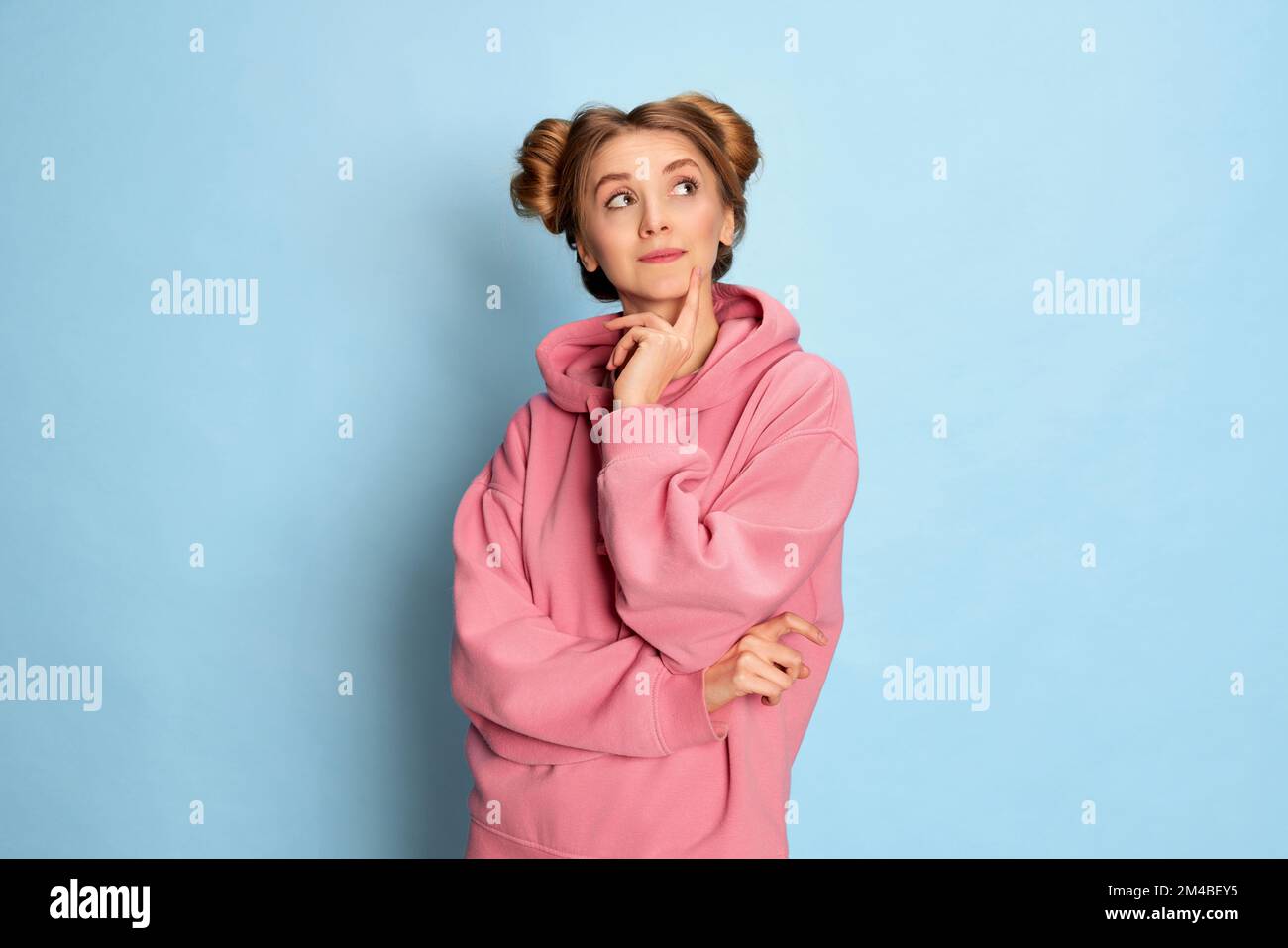 Portrait of young girl in pink hoodie posing with dreamy face over blue ...